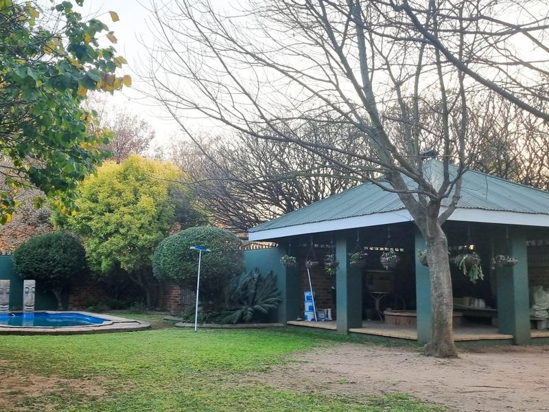 A spacious backyard featuring a swimming pool, a covered patio area, and established garden landscaping with mature trees.