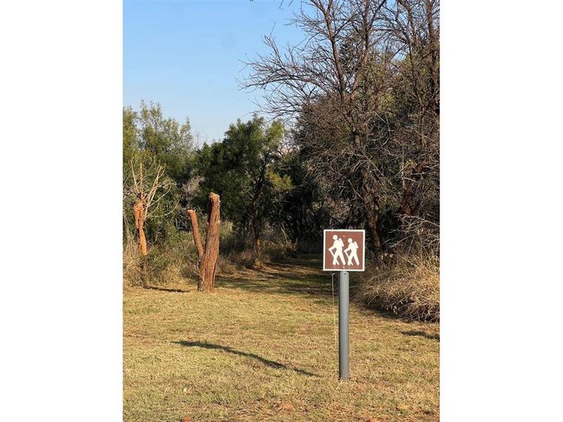 A view of the vacant residential land featuring natural vegetation and a pedestrian path sign.