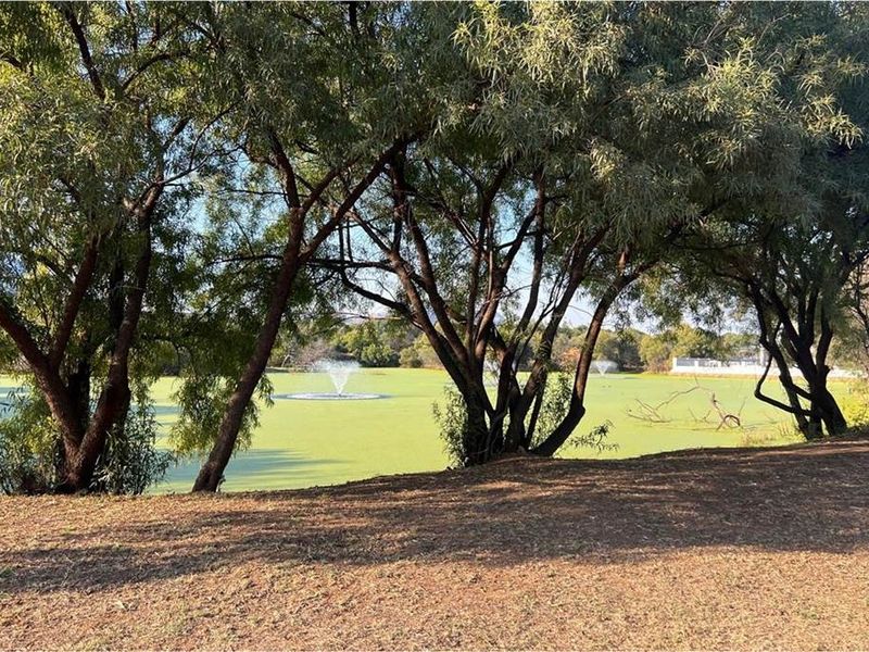 A scenic view of a tranquil lake featuring a water fountain, framed by mature trees on the property grounds.