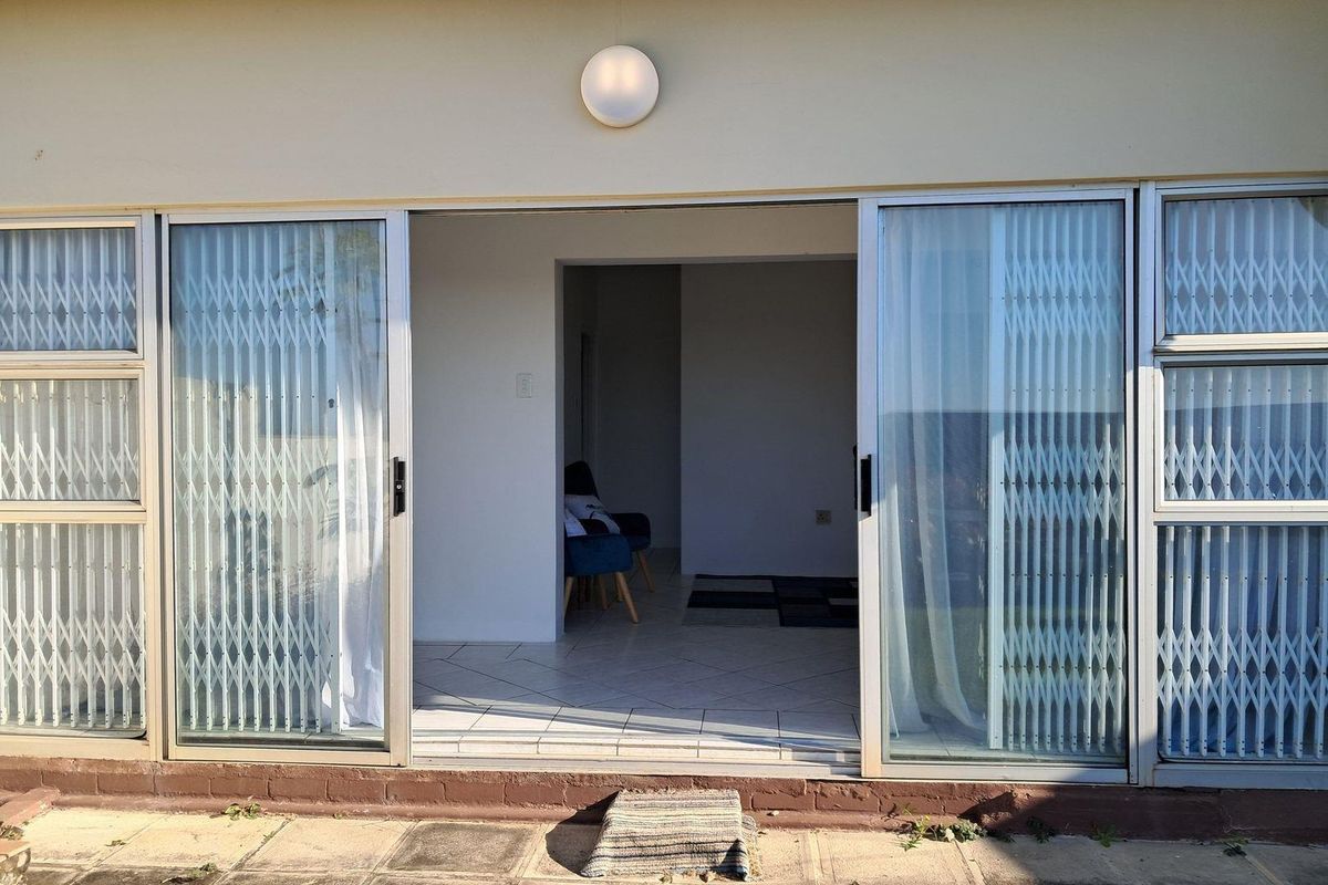 A ground-level apartment entrance featuring sliding glass doors with security gates, leading into a tiled interior living space.
