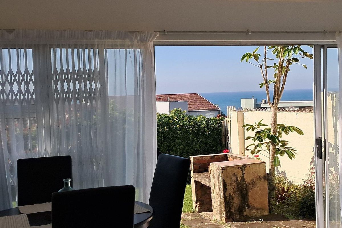 A view from an interior living space looking out onto a patio area featuring a built-in brick braai and ocean views.