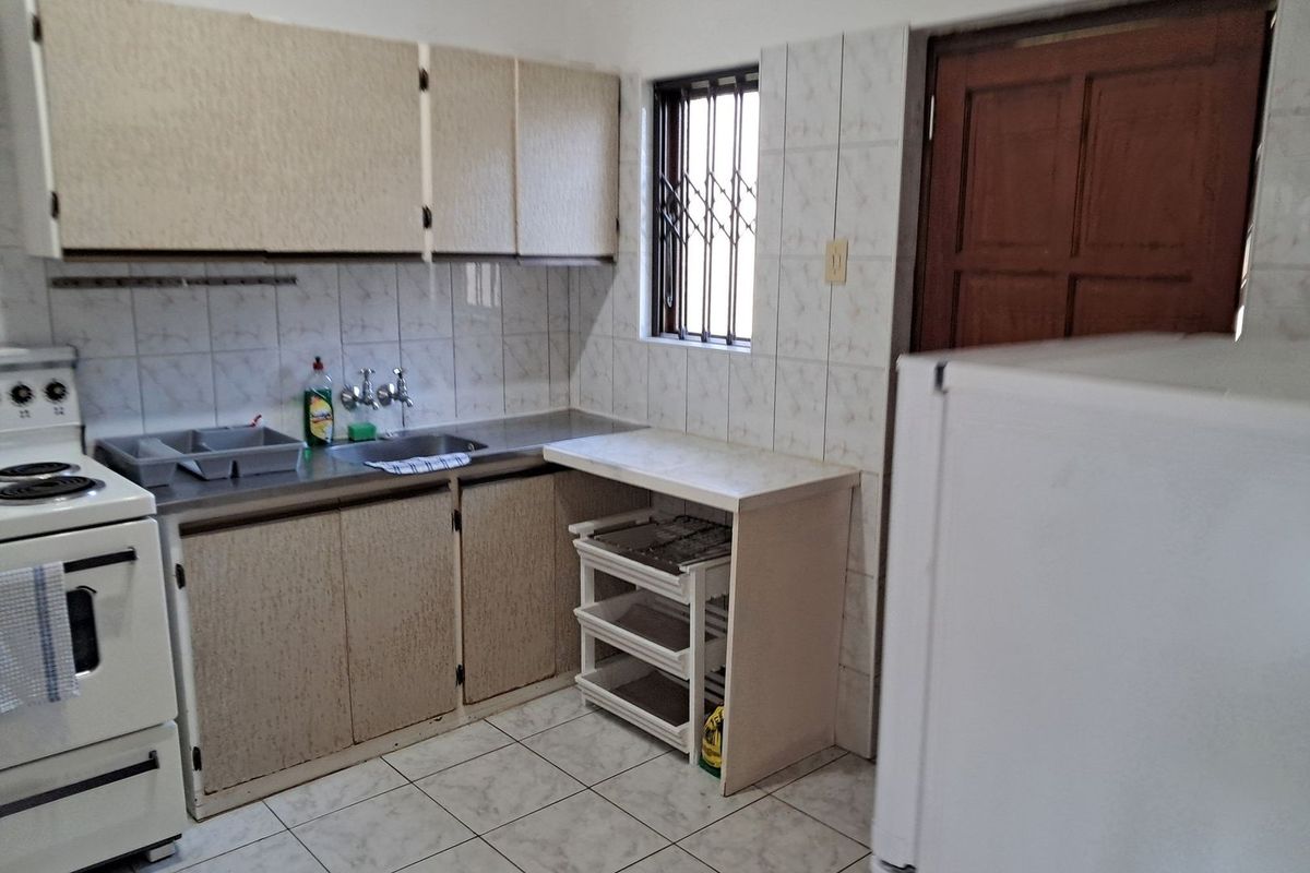 A functional kitchen featuring built-in cabinetry, a stainless steel sink, tiled splashbacks, and a freestanding stove, with a window providing natural light.