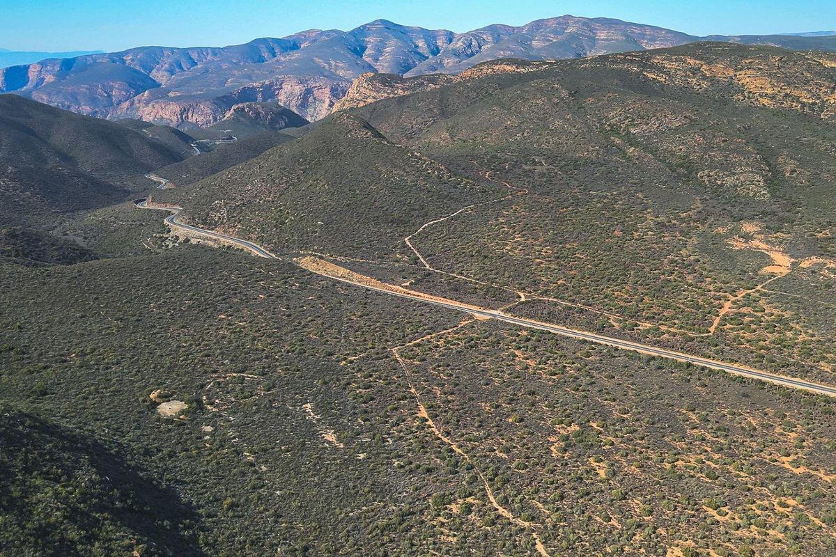 An expansive aerial view of the rugged mountain landscape and surrounding natural terrain, showcasing the vast rural setting of the property.