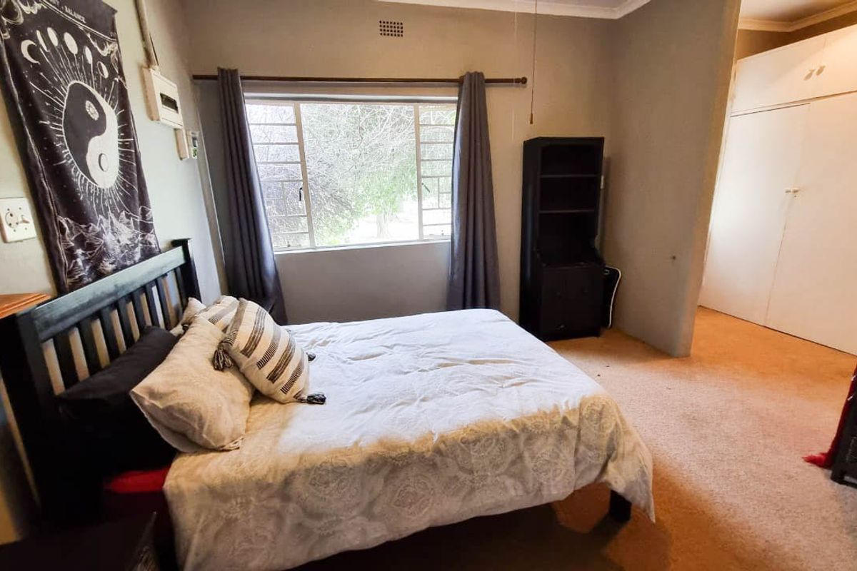 A functional bedroom featuring built-in cupboards, carpeted flooring, and a steel-framed window providing natural light.