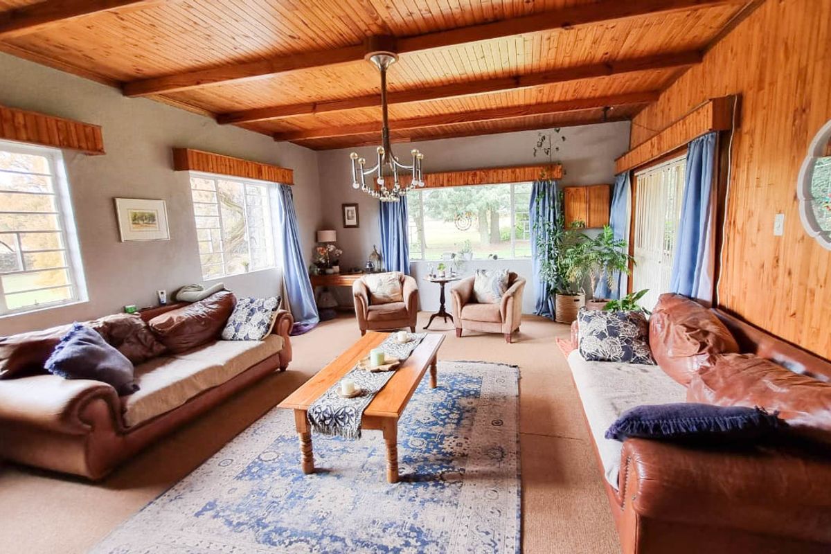 Spacious living room featuring warm timber wall paneling, exposed beam ceilings, and large windows providing ample natural light and garden views.
