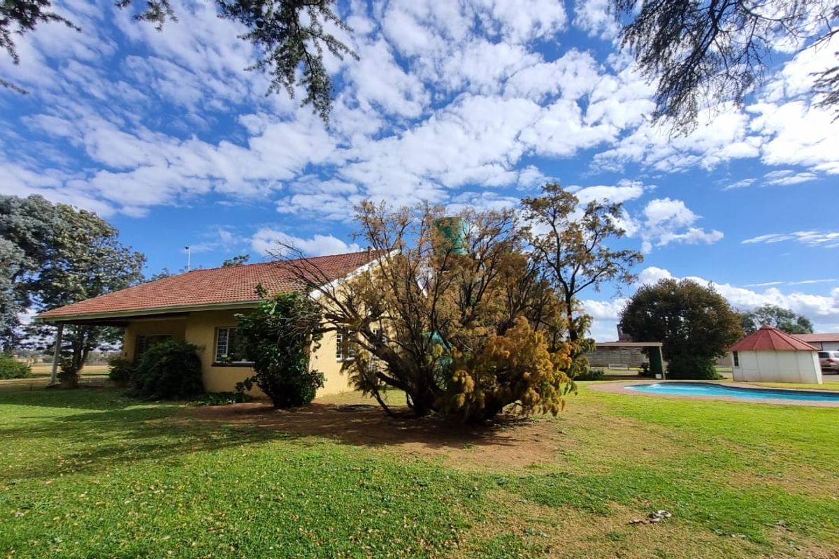 Rear view of the farmhouse featuring a covered patio, swimming pool, and established garden with a water tank.