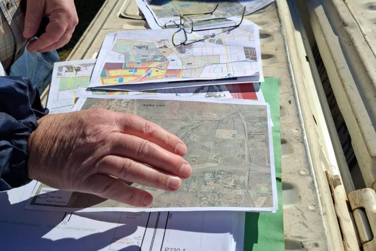 A collection of land development plans and aerial maps displayed on the tailgate of a vehicle, detailing the layout of Rama City.