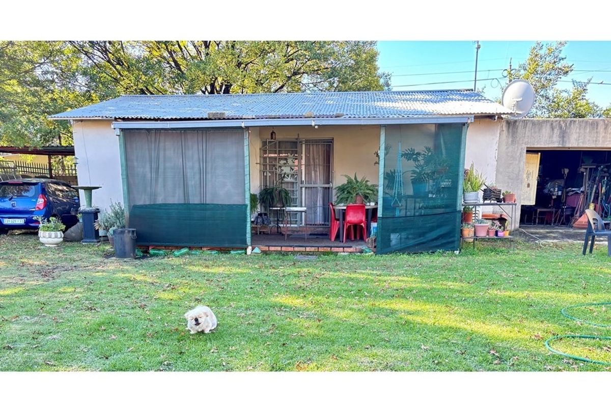 Rear view of the property featuring a covered patio area with shade netting, corrugated iron roofing, and access to the garden.