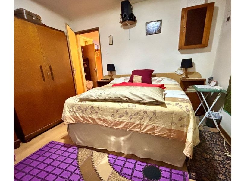A compact bedroom featuring laminate flooring and built-in storage, providing a functional sleeping space with direct access to an adjoining room.