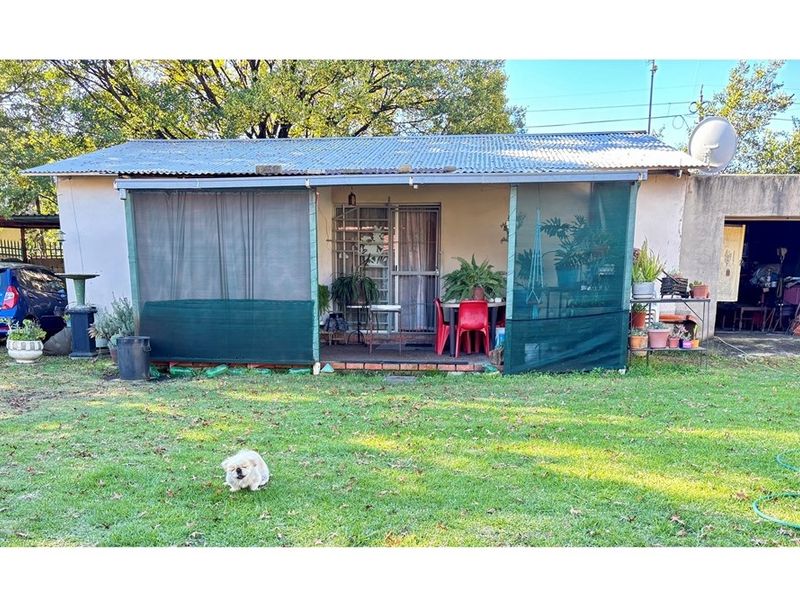Rear view of the property featuring a covered patio area with shade netting, corrugated iron roofing, and access to the garden.
