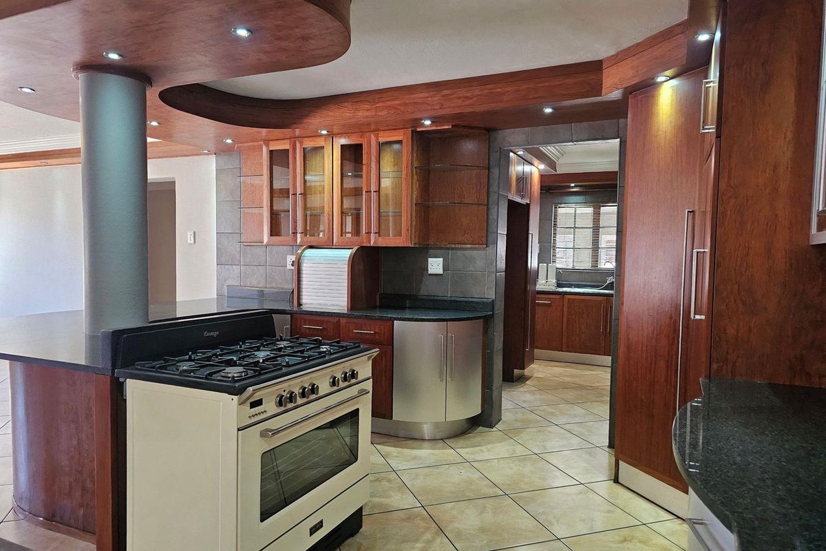 Spacious kitchen featuring custom wood cabinetry, granite countertops, a gas range, and a breakfast bar, with an adjacent scullery area.
