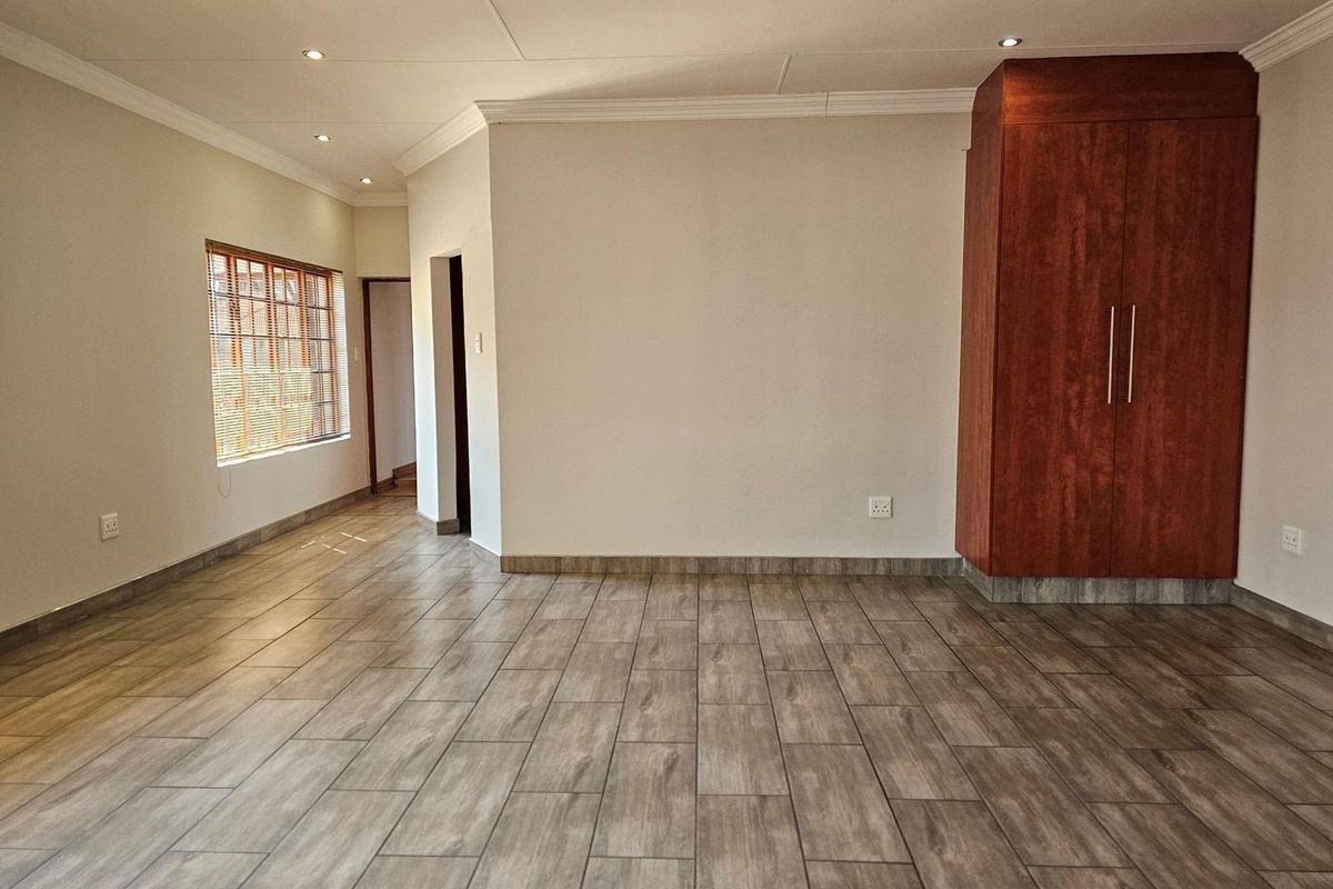 A bright, empty bedroom featuring wood-look tiled flooring, recessed ceiling lighting, and a built-in wooden wardrobe.
