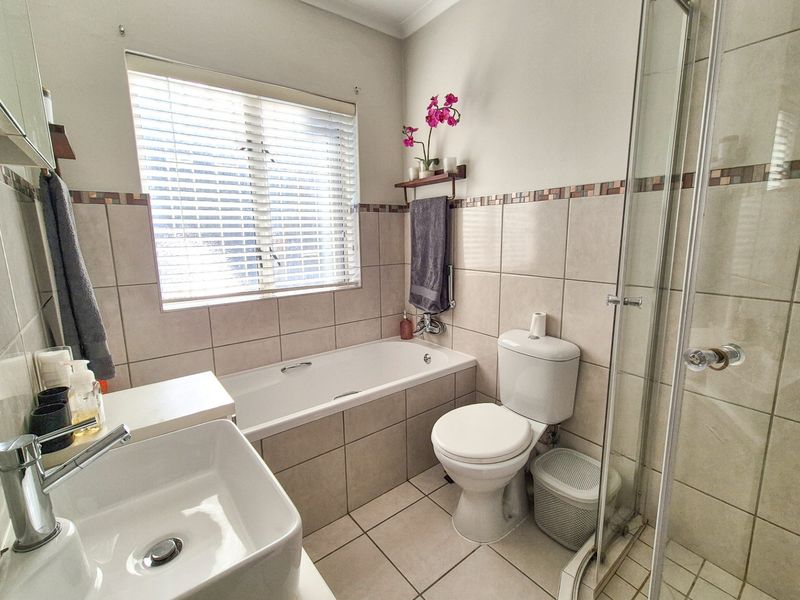 A well-maintained bathroom featuring a built-in bathtub, separate glass shower enclosure, ceramic tiling, and a modern basin with chrome fixtures.