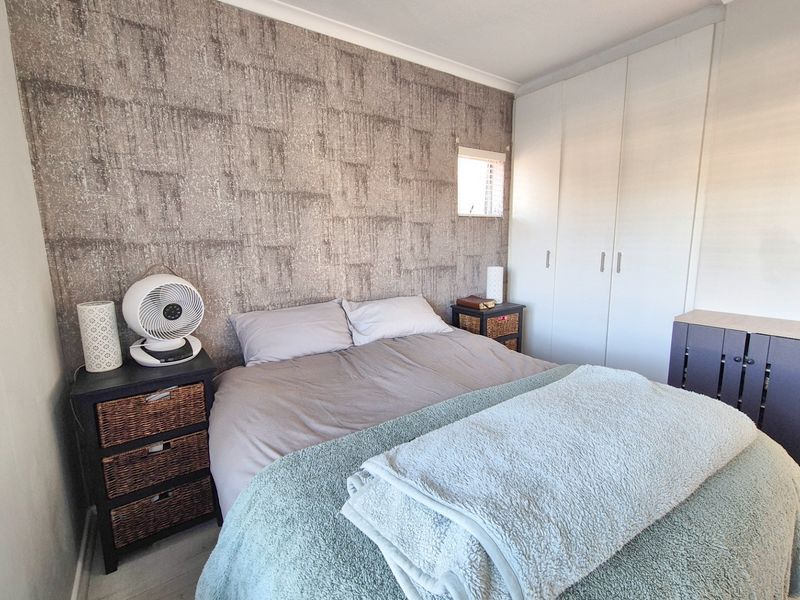 A bedroom featuring built-in wardrobes and a textured feature wall, providing a functional and neutral sleeping space.