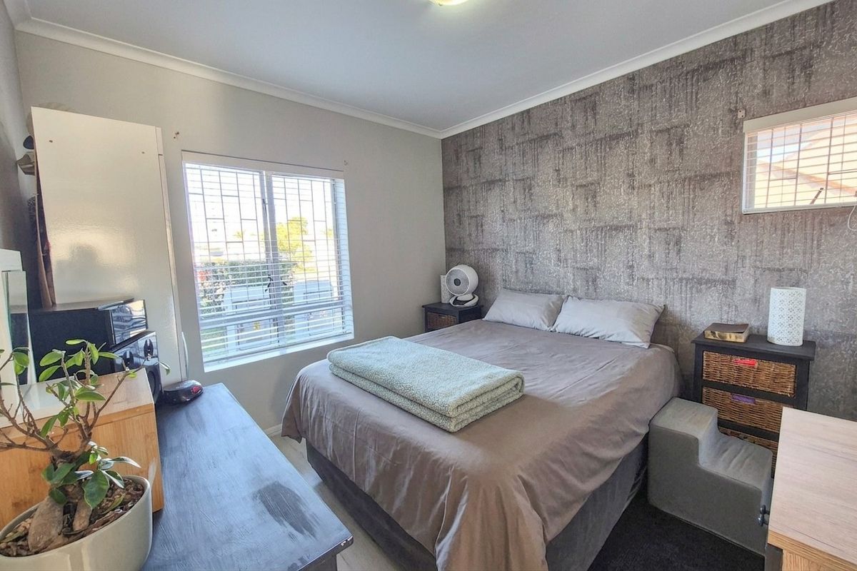 A bedroom featuring a textured accent wall, security bars on the window, and venetian blinds.