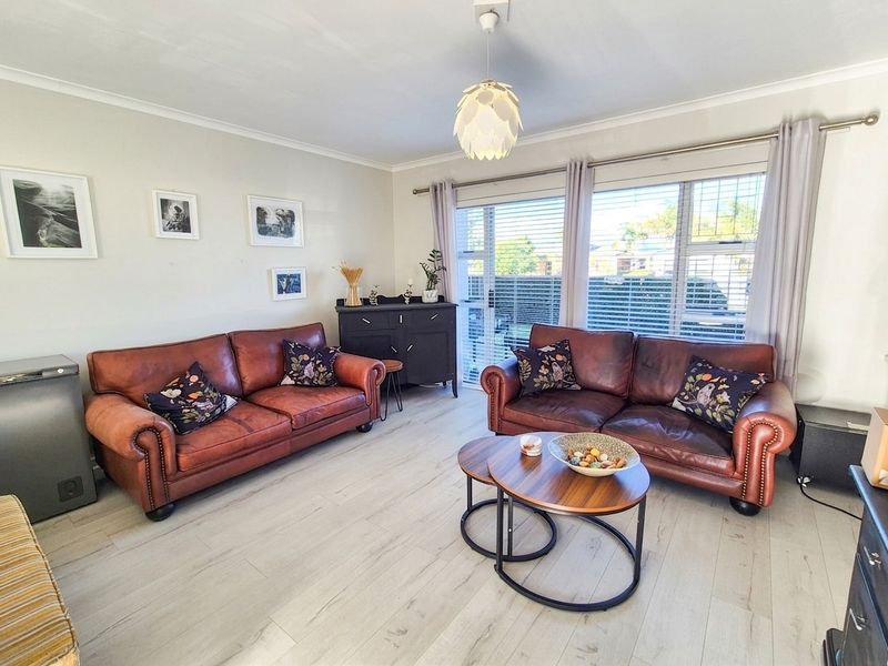 A bright and well-maintained living room featuring light-toned laminate flooring, a modern pendant light, and large sliding glass doors providing natural light.