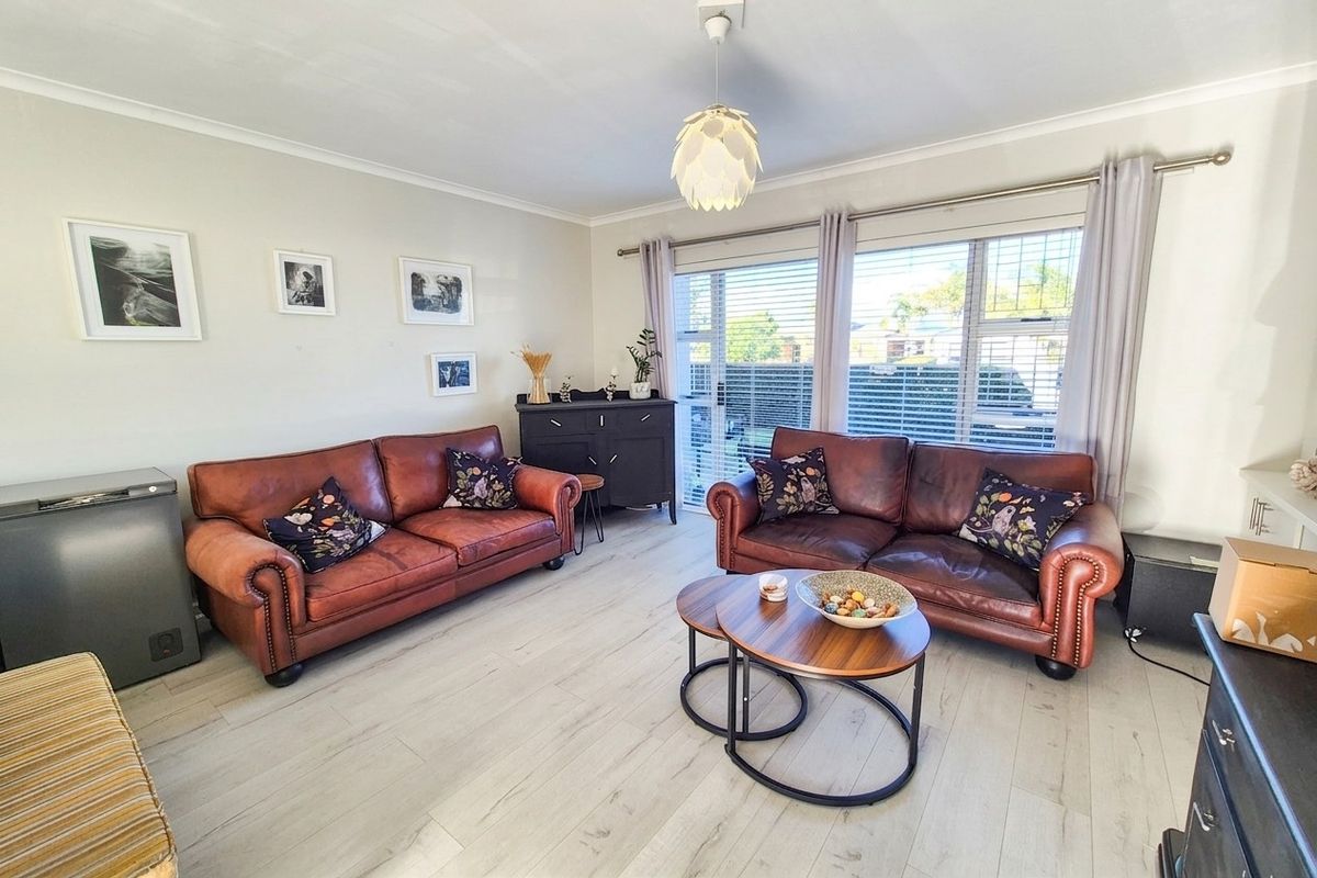 A bright and well-maintained living room featuring light-toned laminate flooring, a modern pendant light, and large sliding glass doors providing natural light.