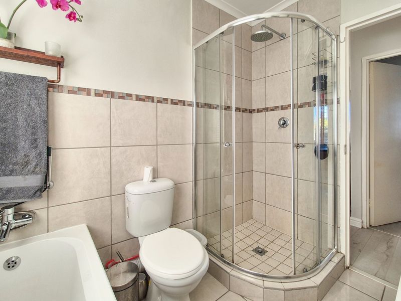 A well-maintained bathroom featuring a corner shower enclosure, a bathtub, a toilet, and neutral wall and floor tiling.