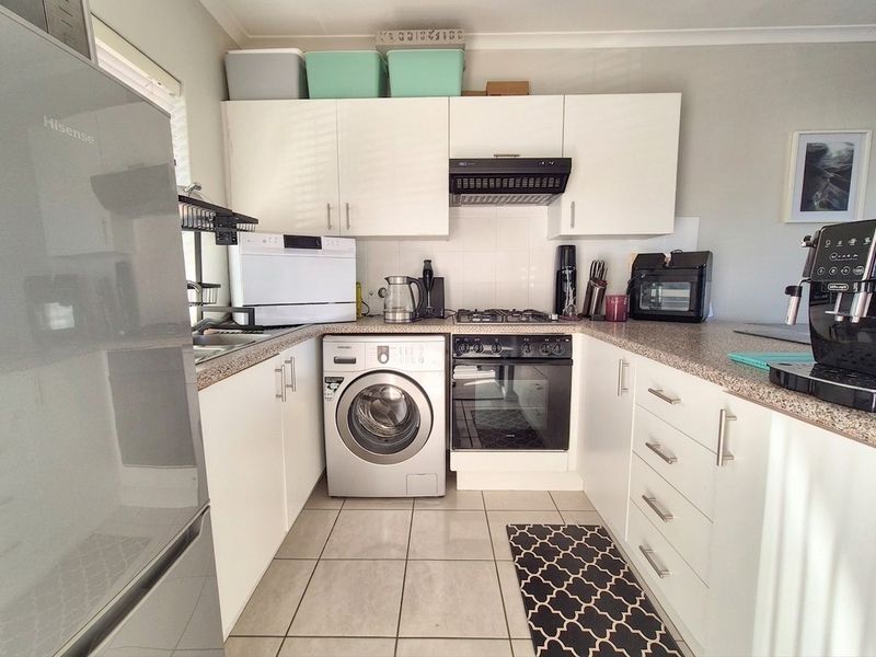 Compact kitchen featuring white cabinetry, laminate countertops, built-in oven with gas hob, extractor fan, and tiled flooring.