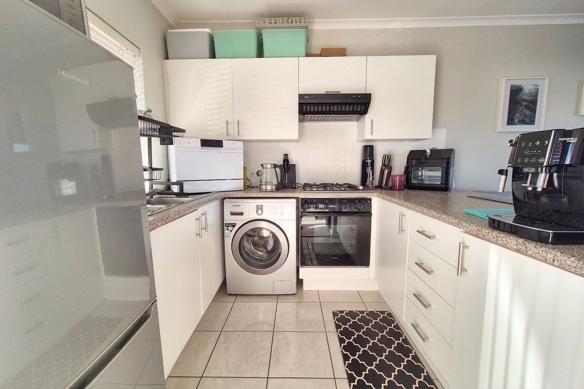 Compact kitchen featuring white cabinetry, laminate countertops, built-in oven with gas hob, extractor fan, and tiled flooring.