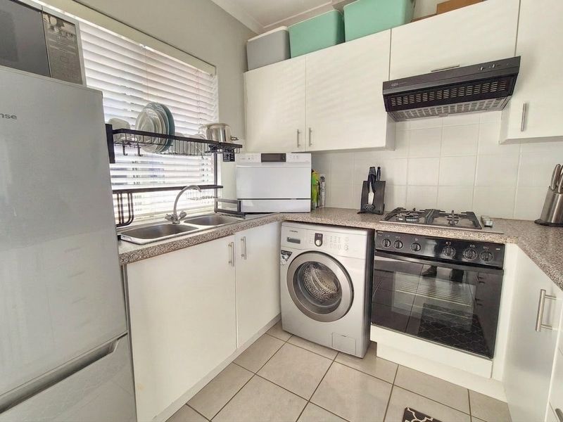 Compact kitchen featuring white cabinetry, laminate countertops, built-in oven with gas hob, extractor fan, and tiled flooring.
