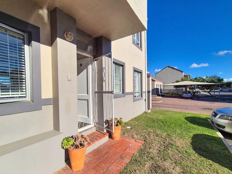 Front entrance of the apartment featuring a security gate, brick paved walkway, and exterior wall lighting.