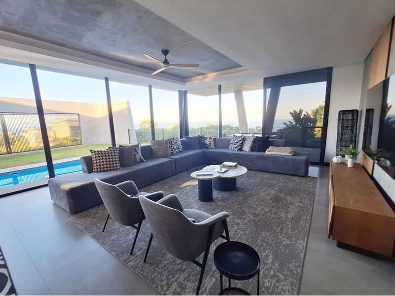 Modern living room featuring expansive floor-to-ceiling glass doors, a recessed ceiling with a fan, and seamless access to the outdoor pool area.