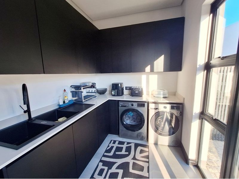 Modern laundry room featuring sleek black cabinetry, stone countertops, an undermount sink, and dedicated space for laundry appliances with natural light.