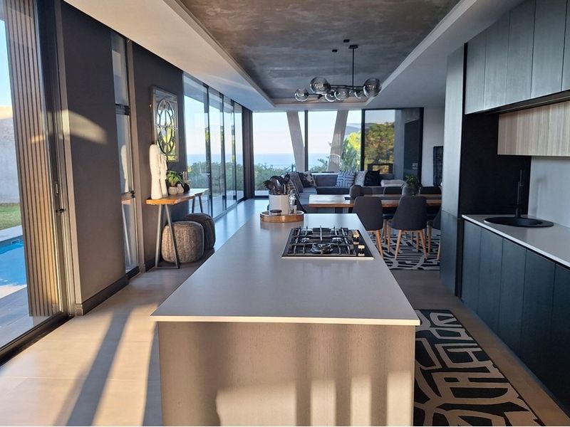 Modern open-plan living area featuring a sleek kitchen island with gas cooktop, expansive sliding glass doors, and seamless flow to the outdoor pool area.