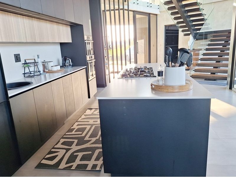 Modern kitchen featuring a central island with gas cooktop, sleek cabinetry, and an adjacent floating staircase with glass balustrade.