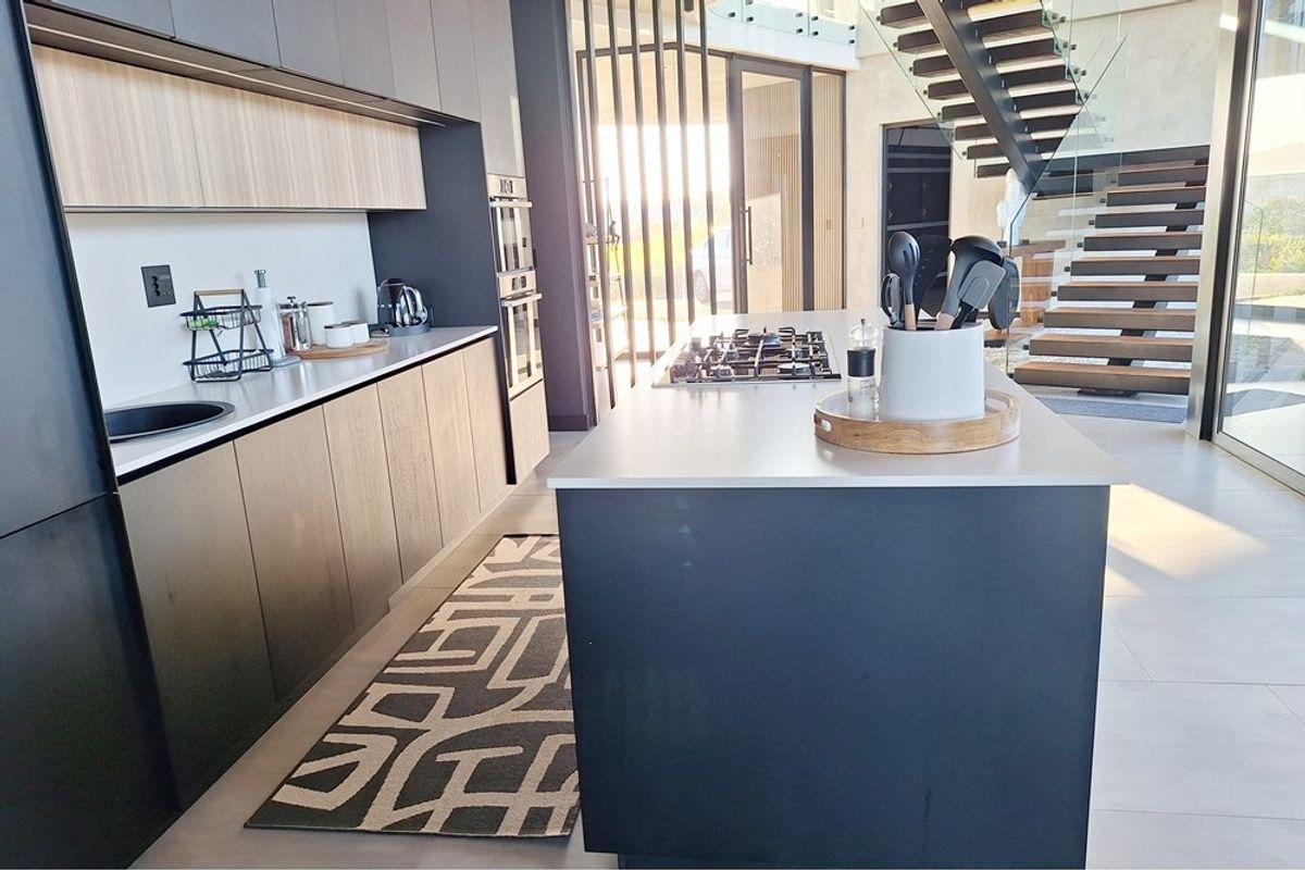 Modern kitchen featuring a central island with gas cooktop, sleek cabinetry, and an adjacent floating staircase with glass balustrade.
