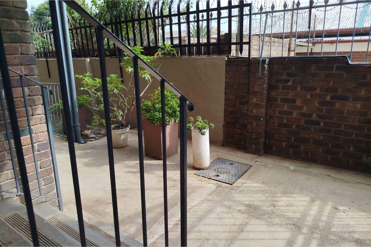 A paved rear courtyard area featuring brick boundary walls, metal security fencing, and a metal staircase railing.