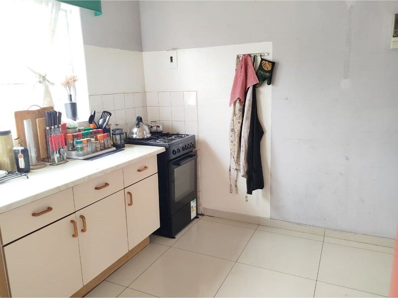A functional kitchen featuring built-in cabinetry, a gas stove, tiled backsplash, and tiled flooring, currently requiring cosmetic updates to the wall finishes.