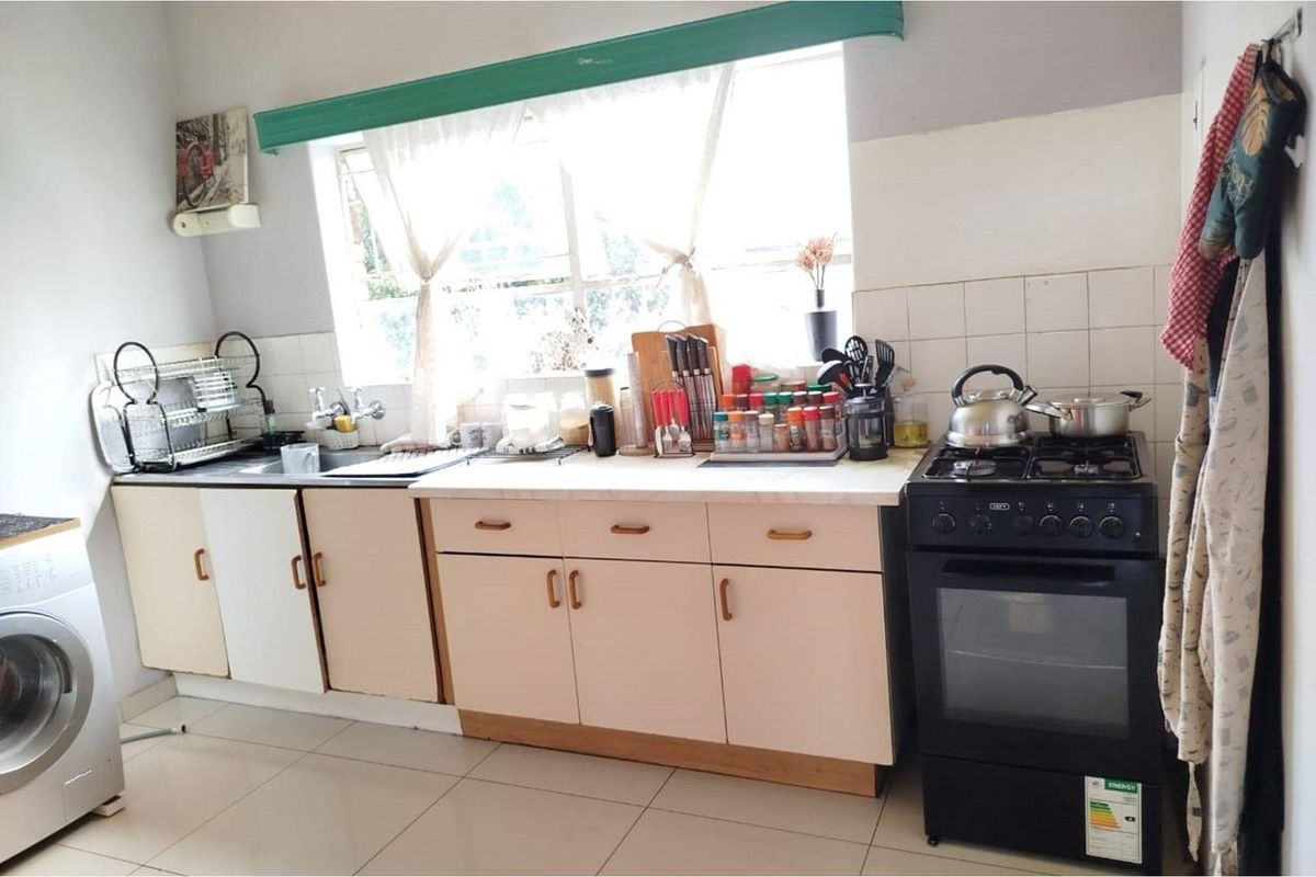 A functional kitchen featuring laminate countertops, built-in cabinetry, a tiled backsplash, and a freestanding stove with tiled flooring throughout.