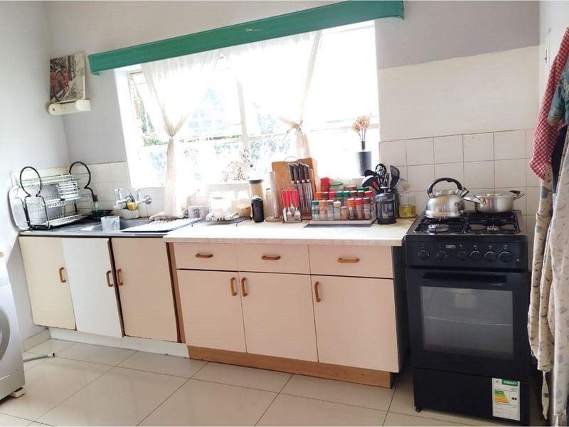 A functional kitchen featuring laminate countertops, built-in cabinetry, a tiled backsplash, and a freestanding stove with tiled flooring throughout.