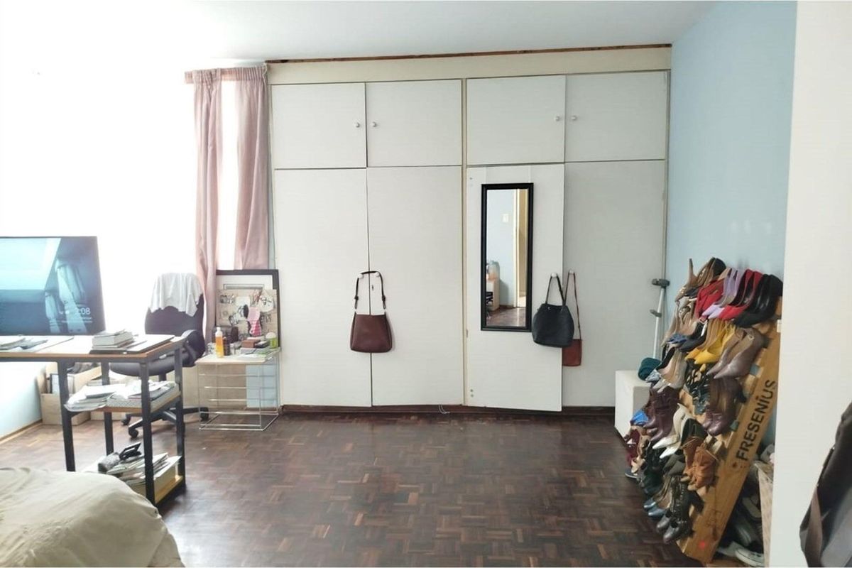 Bedroom featuring classic parquet flooring and extensive built-in cupboard storage, offering a functional layout with potential for cosmetic updates.