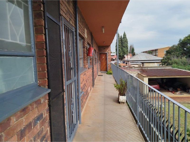 An exterior apartment balcony featuring brick walls, metal security gates, and a metal balustrade overlooking the surrounding property.