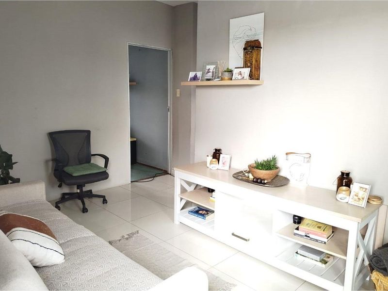 A well-maintained living room featuring neutral wall tones, light-colored tiled flooring, and a functional floating wall shelf.