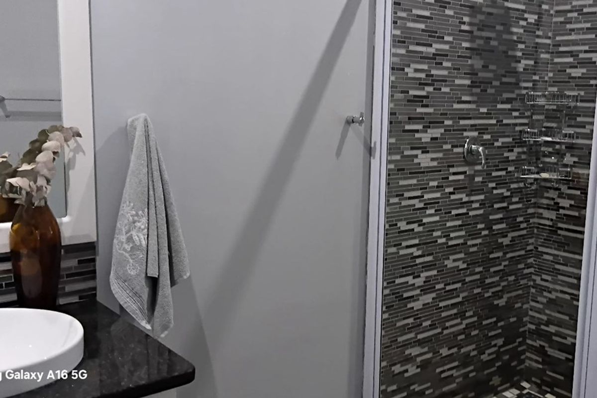 A modern bathroom featuring a walk-in shower with decorative mosaic tiling, a dark granite vanity countertop, and a contemporary vessel sink.