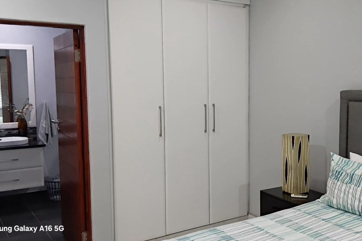 Bedroom featuring built-in cupboards and an adjoining en-suite bathroom with a modern vanity unit.