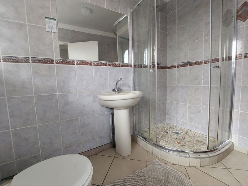 A functional bathroom featuring a pedestal basin, a glass-enclosed corner shower with pebble-style flooring, and neutral wall tiling.
