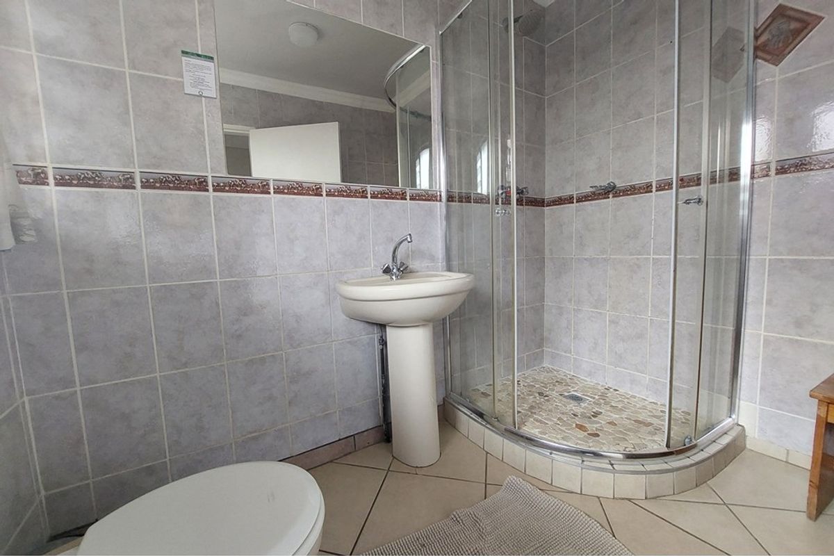 A functional bathroom featuring a pedestal basin, a glass-enclosed corner shower with pebble-style flooring, and neutral wall tiling.