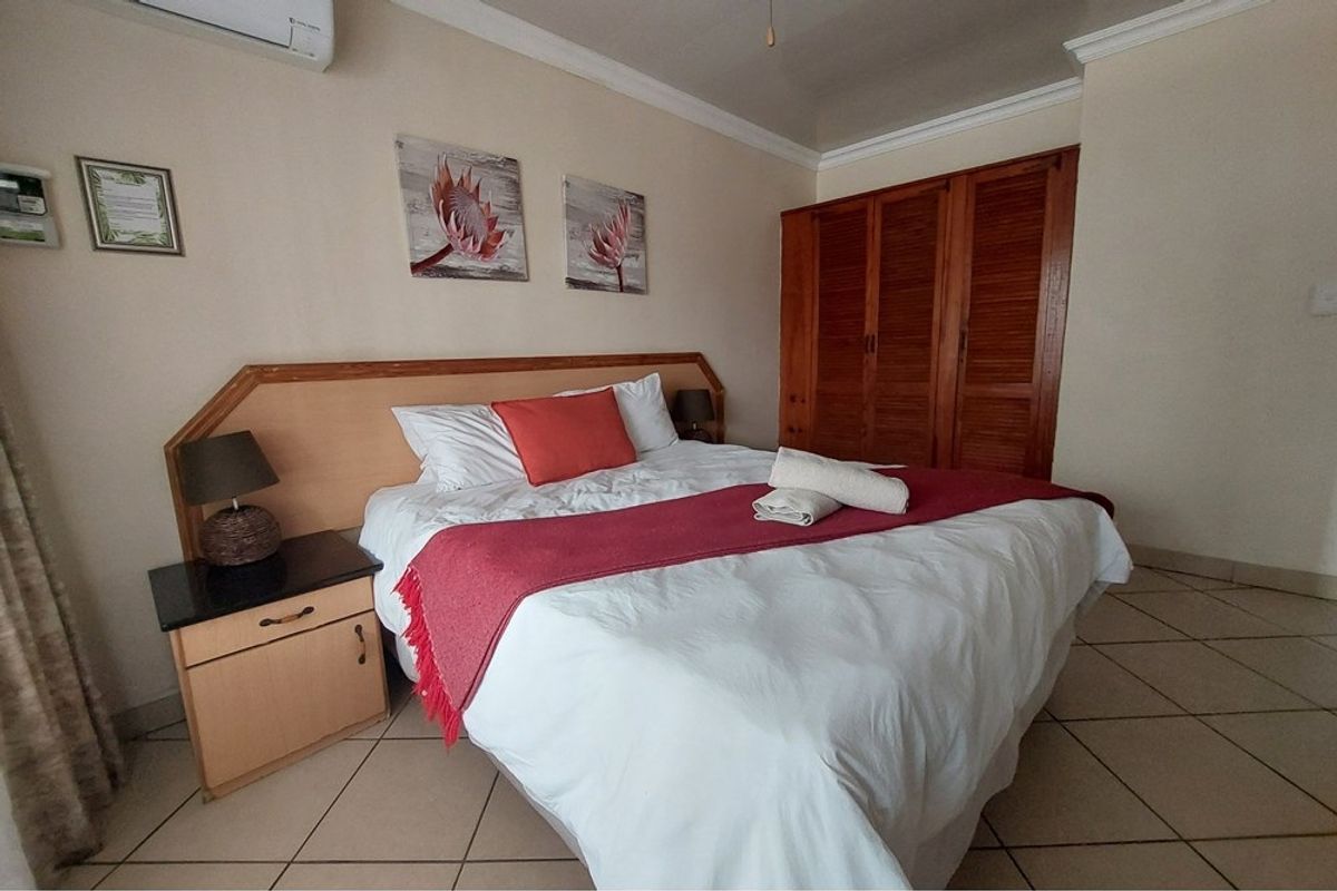 A bedroom featuring tiled flooring, built-in wooden cupboards, and a wall-mounted air conditioning unit.