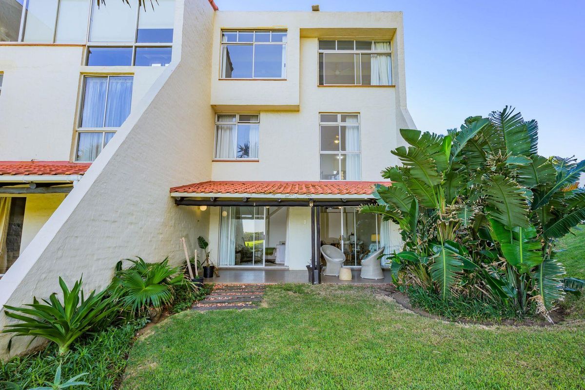 Rear view of a multi-level townhouse featuring a covered patio, sliding glass doors, and a private garden area.
