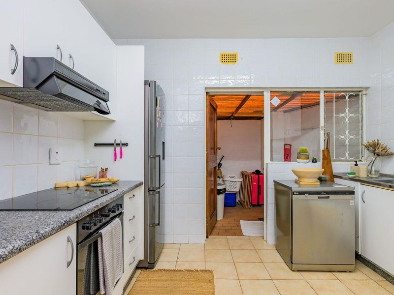 Functional kitchen featuring white cabinetry, granite countertops, built-in oven, electric hob, and tiled finishes, with direct access to an adjacent utility area.
