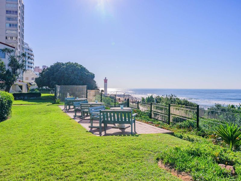 Scenic coastal view featuring a landscaped lawn, paved patio area, and metal fencing overlooking the ocean and lighthouse.