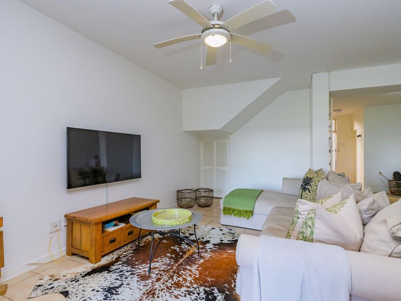 A comfortable living room featuring tiled flooring, a ceiling fan, and convenient built-in under-stair storage.