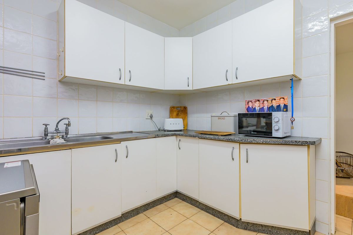 A functional kitchen featuring white laminate cabinetry, granite countertops, a stainless steel sink, and tiled backsplash with ceramic flooring.
