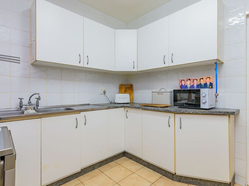A functional kitchen featuring white laminate cabinetry, granite countertops, a stainless steel sink, and tiled backsplash with ceramic flooring.
