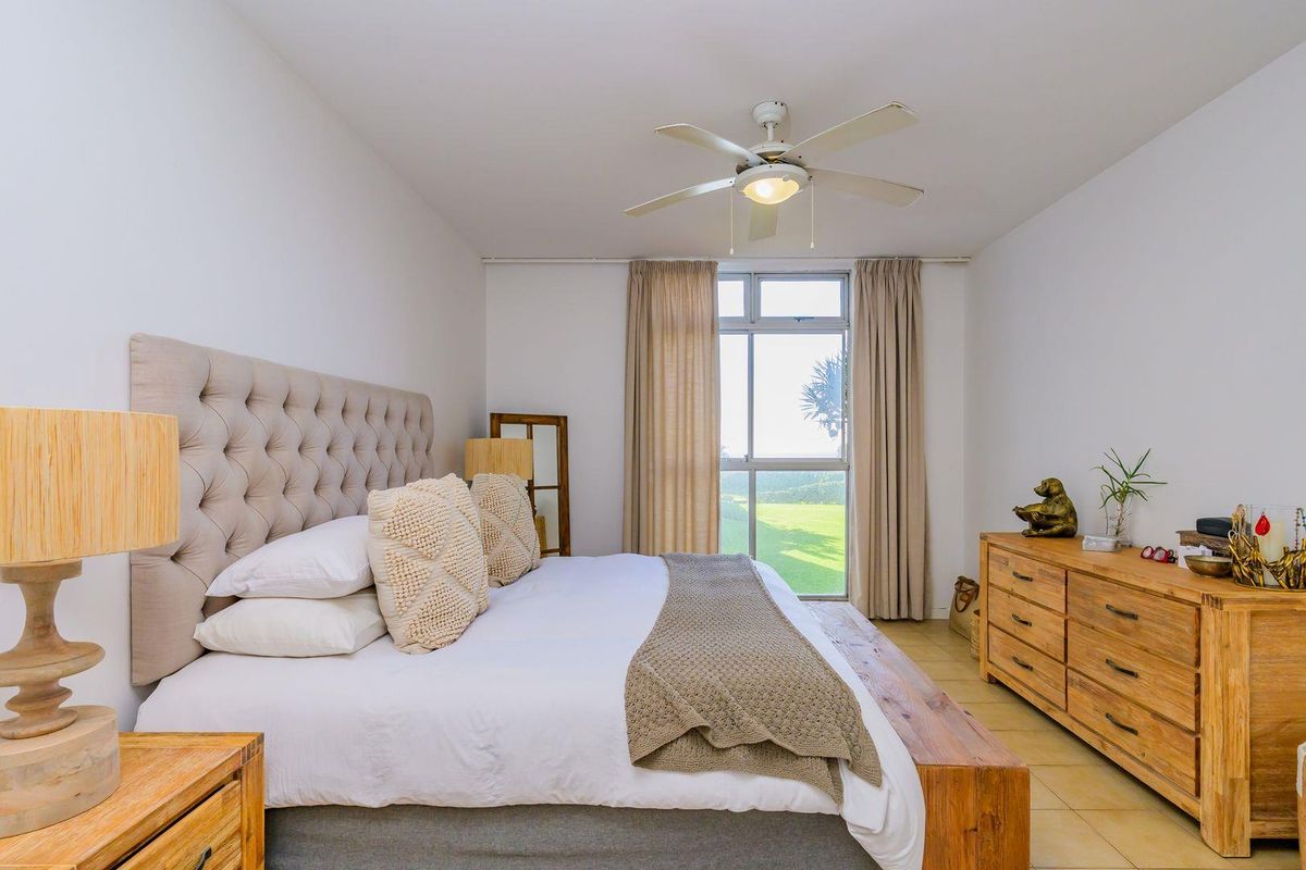 A well-lit bedroom featuring tiled flooring, a ceiling fan, and a large window with views of the surrounding landscape.